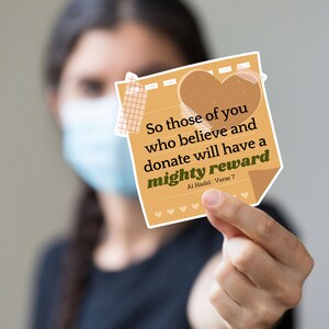 May include: A tan-colored sticky note with rounded corners and a heart shape at the top. The note has a quote in black text that reads "So those of you who believe and donate will have a mighty reward Al Hadid: Verse 7".