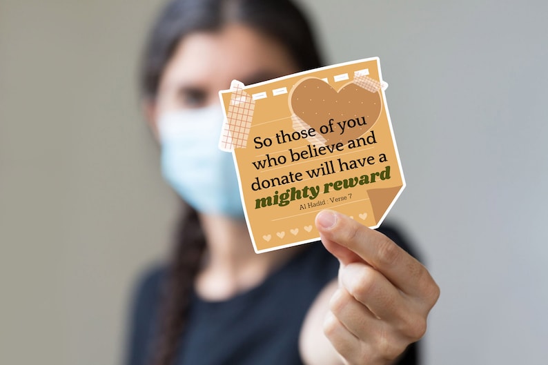 May include: A tan-colored sticky note with rounded corners and a heart shape at the top. The note has a quote in black text that reads "So those of you who believe and donate will have a mighty reward Al Hadid: Verse 7".