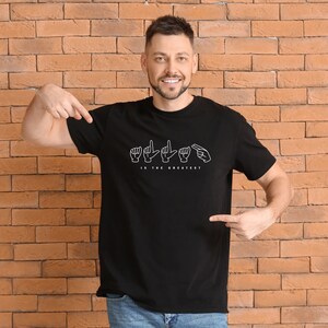 May include: A black t-shirt with a white graphic of the sign language alphabet for the word "LOVE" and the text "IS THE GREATEST".