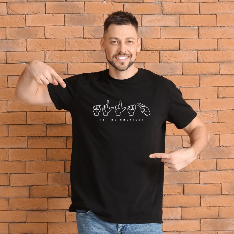 May include: A black t-shirt with a white graphic of the sign language alphabet for the word "LOVE" and the text "IS THE GREATEST".