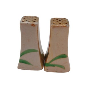 K&ouml;nnte beinhalten: Ein Paar vintage Salz- und Pfefferstreuer mit einem rosa-wei&szlig;en Sockel und gr&uuml;nen und goldenen Akzenten. Die Streuer haben eine einzigartige Form und sind mit einem Blumendesign verziert.