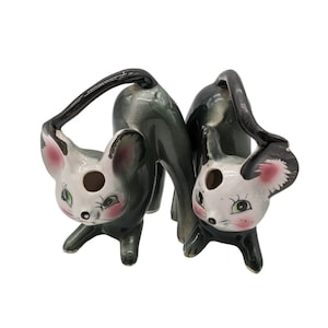 May include: Two black and green ceramic mice figurines with white faces and pink accents. The mice are posed in a playful manner, with their tails curled up.