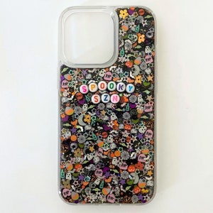 May include: A clear phone case with a black background and colorful glitter. The glitter includes stars, ghosts, pumpkins, and candy corn. The words "SPOOKY SZN" are spelled out in colorful letters.
