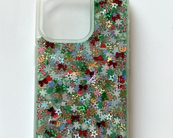 May include: A clear phone case with a glittery design featuring a variety of Christmas-themed shapes, including stars, candy canes, snowflakes, and bows. The glitter is in shades of green, red, gold, and white.