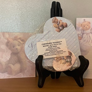 May include: A set of three heart-shaped notepads featuring a teddy bear design. The notepads are blue and white with a pink heart-shaped magnet. The magnet features a teddy bear design and the text "Cherished Teddies™ Magnet with Note Pad Code 94323".