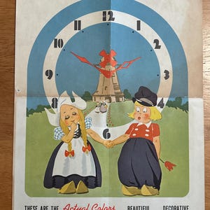 May include: Vintage print featuring a Dutch mill clock design with a blue and white clock face. Two children in traditional Dutch attire are holding hands. The text reads "Actual Size of Your Dutch Mill Clock".