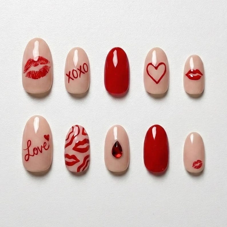 May include: A set of ten artificial nails in various designs. The nails feature a nude base with red lip and heart designs, the word "Love", and the letters "XOXO". Two nails are solid red, and one has a red jewel.