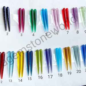 May include: A collection of 22 pairs of colorful, elongated, and pointed glass pendants. The pendants vary in color, including shades of brown, blue, green, red, purple, yellow, and clear. Each pair is displayed side-by-side, showcasing their unique hues and textures.