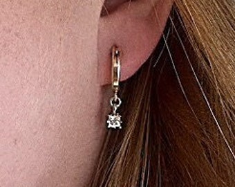 May include: A close-up of a person's ear wearing a gold hoop earring with a small diamond dangling from it.