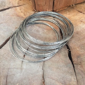 Op de afbeelding: Een stapel zilveren armbanden met een gehamerde textuur. De armbanden zijn op elkaar gestapeld en in een cirkel gerangschikt.