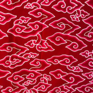 May include: A close-up of a red fabric with a repeating cloud pattern. The clouds are outlined in white and filled with shades of pink and red. The design is a traditional batik style.