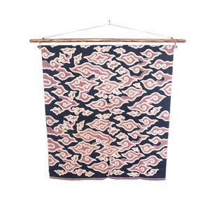 May include: A dark blue fabric wall hanging with a repeating cloud pattern in shades of pink and cream. The fabric is suspended from a wooden rod with a metal wire for hanging. The design is symmetrical and detailed.