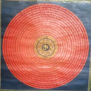 Puede incluir: Un mandala circular con fondo rojo y letras doradas. El centro del mandala presenta un c&iacute;rculo negro con un s&iacute;mbolo dorado y un borde dorado. El mandala est&aacute; rodeado de c&iacute;rculos conc&eacute;ntricos de letras doradas.