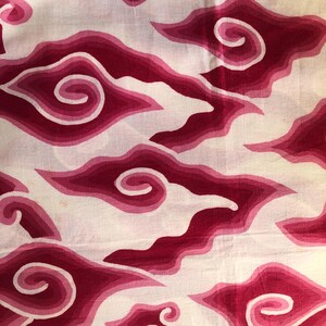 Może przedstawiać: Biała tkanina z powtarzającym się wzorem stylizowanych kształtów chmur w odcieniach różu i czerwieni. Chmury mają efekt warstwowy z wirującym wzorem pośrodku.