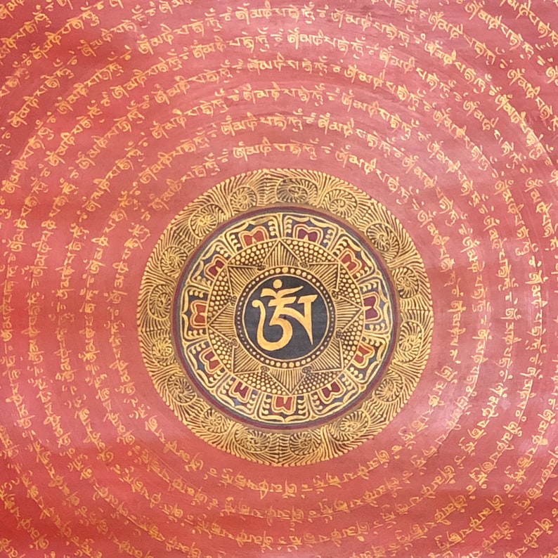 Puede incluir: Un mandala circular rojo con acentos dorados y negros. El mandala presenta un s&iacute;mbolo central con el texto "ཨ" en negro y dorado. El mandala est&aacute; rodeado de c&iacute;rculos conc&eacute;ntricos de texto en dorado.