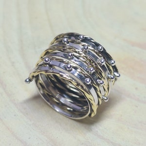 May include: A silver and gold ring with a textured design and small beads. The ring is made of multiple bands that are twisted together.