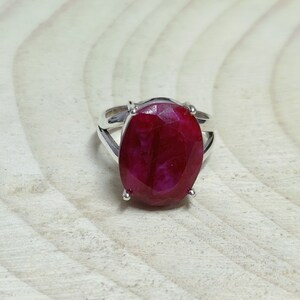 Op de afbeelding: Een zilveren ring met een grote, ovale robijn. De robijn is diep rood van kleur en heeft een licht getextureerd oppervlak.