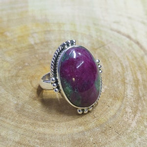 May include: A silver ring featuring a large oval green and pink gemstone set in a beaded bezel.