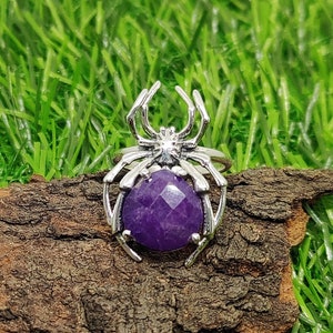 May include: A silver spider ring with a large, faceted amethyst gemstone in the center.