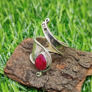 Op de afbeelding: Een zilveren ring met een rode edelsteen gezet in een gedraaide band. De ring is ontworpen om om de vinger te wikkelen.