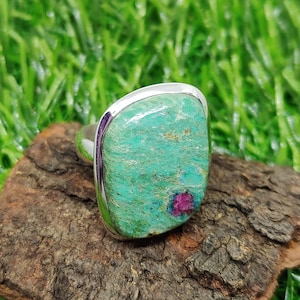 May include: A silver ring with a green and pink gemstone. The gemstone is a rectangular shape with a smooth surface. The ring is set in a silver band.