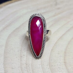 Puede incluir: Un anillo de plata con una piedra preciosa rosa engastada en forma de lágrima. El anillo tiene un diseño detallado de cuerda alrededor del borde del engaste.