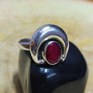 Könnte beinhalten: Ein silberner Ring mit einem roten Edelstein, der in einem Halbmond-Design gefasst ist.