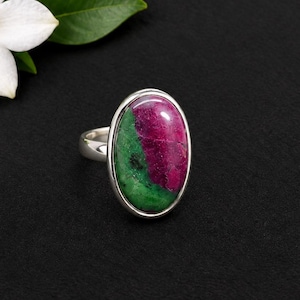 Op de afbeelding: Een zilveren ring met een grote, ovaalvormige cabochonsteen met duidelijke secties van diep magenta en levendig groen. De steen is gezet in een gladde, gepolijste zilveren zetting en de ringband is eveneens vervaardigd uit gepolijst zilver.
