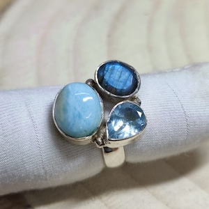 Op de afbeelding: Een zilveren ring met drie blauwe edelstenen. De ring heeft een grote ovale blauwe edelsteen, een kleinere ovale blauwe edelsteen en een ronde blauwe edelsteen.