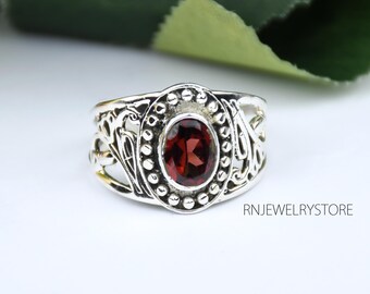 Puede incluir: Un anillo de plata con un diseño adornado que presenta una piedra preciosa roja. El anillo tiene un borde de cuentas alrededor de la piedra preciosa.