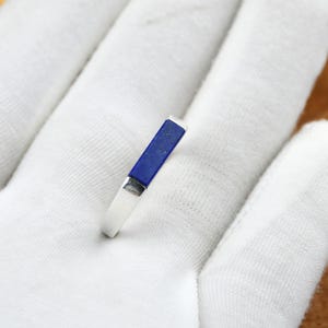 Op de afbeelding: Een zilveren ring met een rechthoekige, diepblauwe lapis lazuli steen. De ring is geplaatst op een witte achtergrond, wat het contrast tussen het heldere metaal en de donkerblauwe steen benadrukt. Het ontwerp van de ring is eenvoudig en elegant.