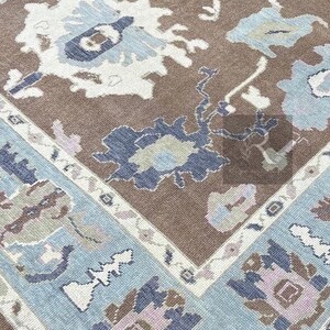 Pu&ograve; includere: Un tappeto marrone con un motivo floreale blu e bianco. Il tappeto ha un bordo blu chiaro con un design geometrico bianco e marrone.
