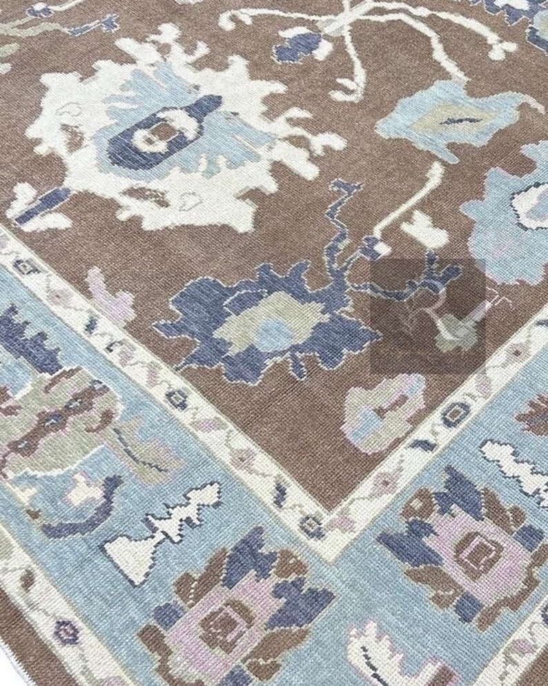 Pu&ograve; includere: Un tappeto marrone con un motivo floreale blu e bianco. Il tappeto ha un bordo blu chiaro con un design geometrico bianco e marrone.