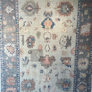 May include: A vintage rug with a beige background and a blue, gray, and pink geometric pattern. The rug has a border with a repeating pattern of triangles and diamonds.