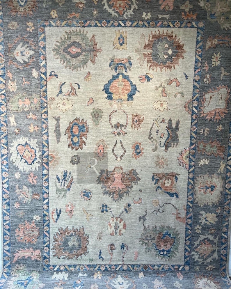 May include: A vintage rug with a beige background and a blue, gray, and pink geometric pattern. The rug has a border with a repeating pattern of triangles and diamonds.