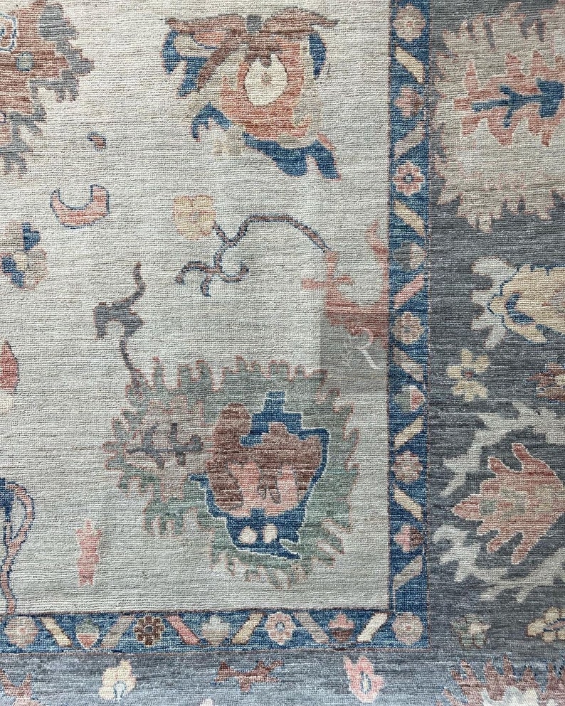 May include: A close-up of a rug with a light beige background and a blue, green, and red floral pattern. The rug has a dark blue border with a geometric pattern.