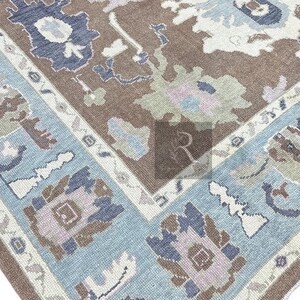 Pu&ograve; includere: Un tappeto vintage con sfondo marrone e bordo blu e bianco. Il tappeto ha un motivo geometrico con una variet&agrave; di colori, tra cui rosa, verde e blu.