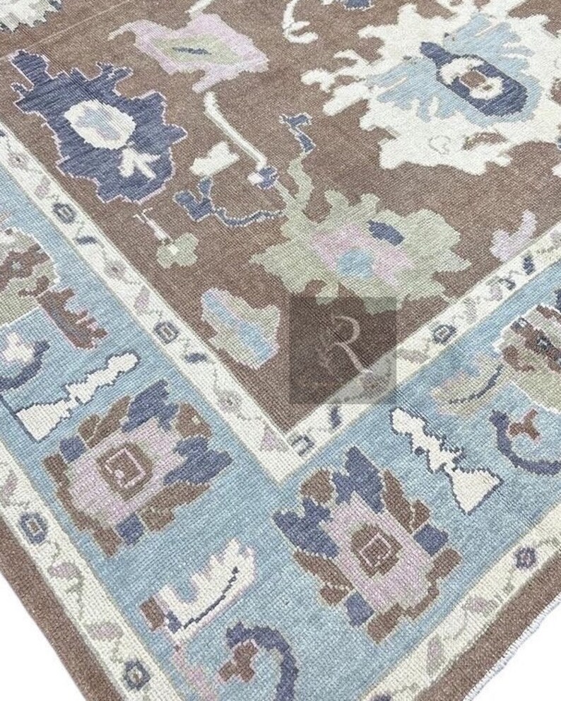 Pu&ograve; includere: Un tappeto vintage con sfondo marrone e bordo blu e bianco. Il tappeto ha un motivo geometrico con una variet&agrave; di colori, tra cui rosa, verde e blu.