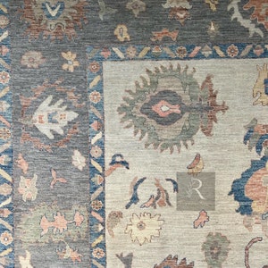 May include: A close-up of a rug with a beige background and a blue, brown, and white patterned design. The rug has a border with a geometric pattern.