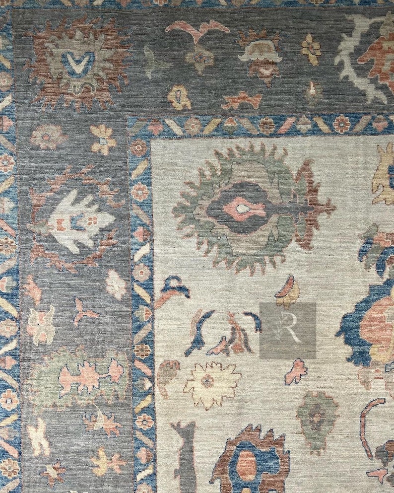 May include: A close-up of a rug with a beige background and a blue, brown, and white patterned design. The rug has a border with a geometric pattern.