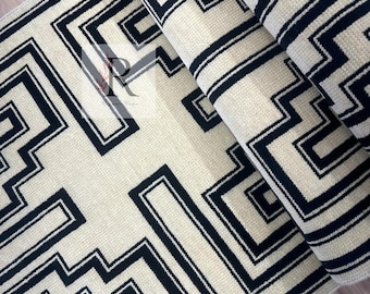May include: A rolled-up rug with a geometric design. The rug features a cream-colored background with a repeating pattern of black angular lines. The rug is made of a woven material and appears to be new.