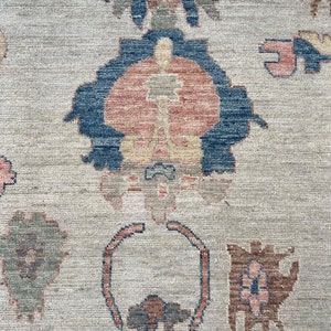May include: A close-up of a beige rug with a repeating pattern of blue, red, and brown floral designs.