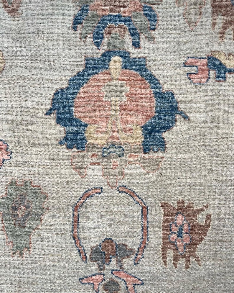 May include: A close-up of a beige rug with a repeating pattern of blue, red, and brown floral designs.