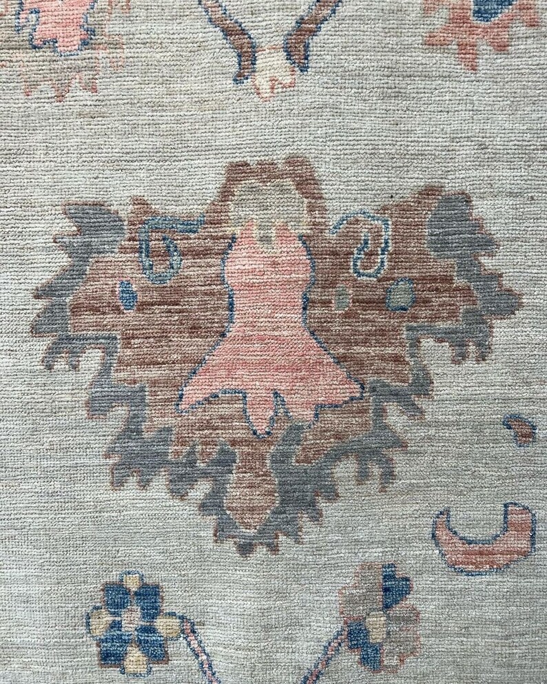 May include: A beige rug with a pink and blue floral pattern. The rug has a traditional design with intricate details.