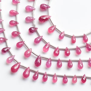 Puede incluir: Una hebra de cuentas de piedras preciosas rosas en forma de lágrima. Las cuentas están enhebradas en alambre plateado.