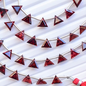 May include: A strand of red gemstone triangle beads on a silver wire with red tassels at each end.