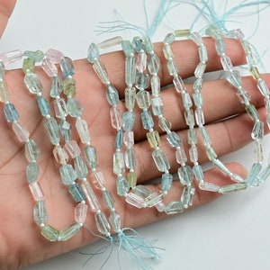 May include: A strand of faceted aquamarine beads in various shades of blue and green. The beads are rectangular in shape and have a smooth, polished finish.
