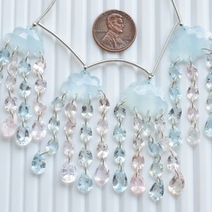 May include: A silver necklace with blue and pink gemstone drops hanging from three cloud-shaped pendants. The necklace is displayed on a white background.