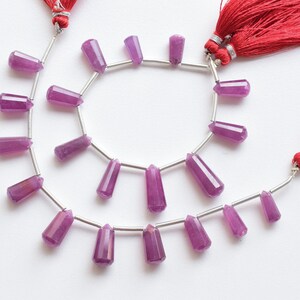May include: A strand of purple gemstone beads with silver connectors. The beads are faceted and have a pointed shape. The strand is strung on a silver chain with two red tassels at the ends.