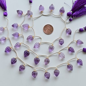 Könnte beinhalten: Eine Strähne aus violetten Amethystperlen mit goldenen Akzenten und einer silbernen Kette. Die Perlen sind tropfenförmig und haben eine facettierte Oberfläche. Die Strähne ist mit violetten Quasten verziert.
